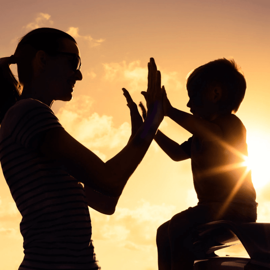 Mother and child high-fiving at sunset, symbolizing connection, trust, and joyful parenting moments.